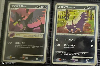 Pair of Japanese Pokémon Cards (Murkrow and Skuntank) in Sleeves