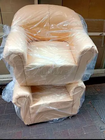 Two cream-colored leather armchairs in plastic wrapping