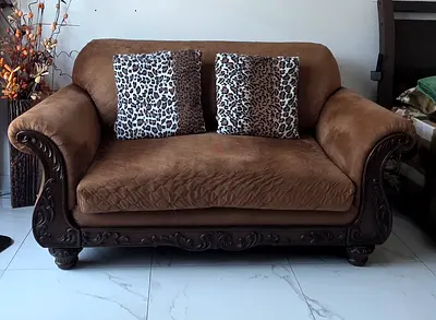 Two-seater brown upholstered sofa with carved wooden frame