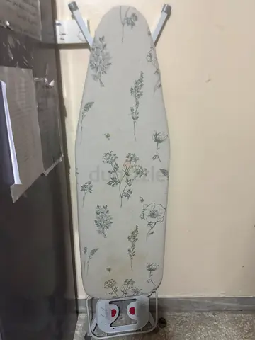 Used ironing board with floral cover and iron rest