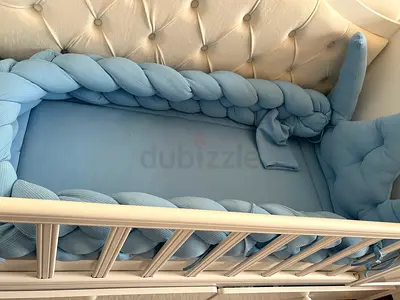 White wooden baby crib with braided bumper and mattress