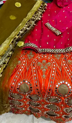 Traditional embroidered lehenga choli set — bright orange skirt with pink blouse and green dupatta
