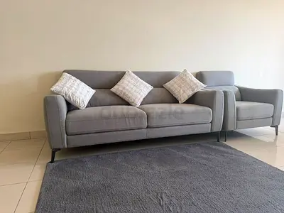 Modern grey 3-seater sofa with single armchair, cushions, and large light shaggy fur carpet