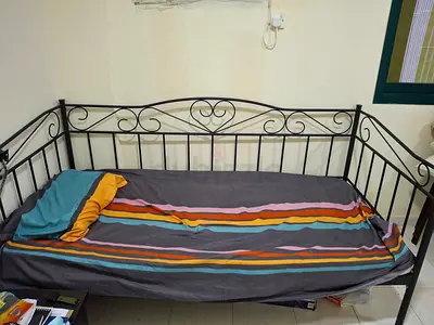 A black metal daybed/single bed with decorative scrollwork on the back and both sides and Mattress