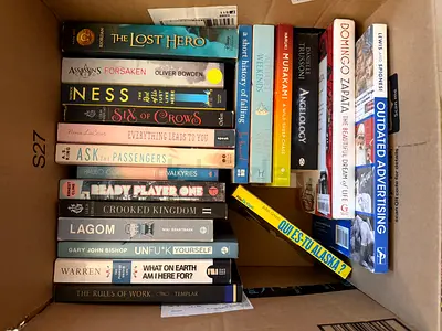 Box of assorted paperback novels and non-fiction books — mixed titles