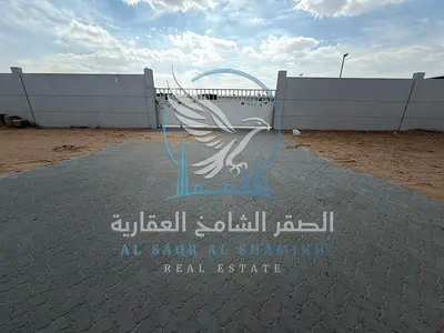 A walled plot of land for rent in Al Sajaa, on a main road, with 25kW electricity and interlocking paving.