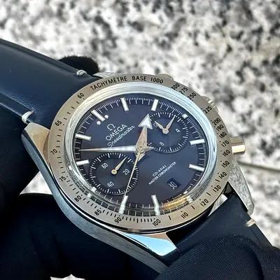 This is an Omega Speedmaster '57 watch featuring a distinctive black dial and a tachymeter bezel.