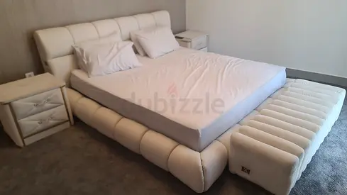 Modern off-white upholstered king bed with bedside tables and ottoman