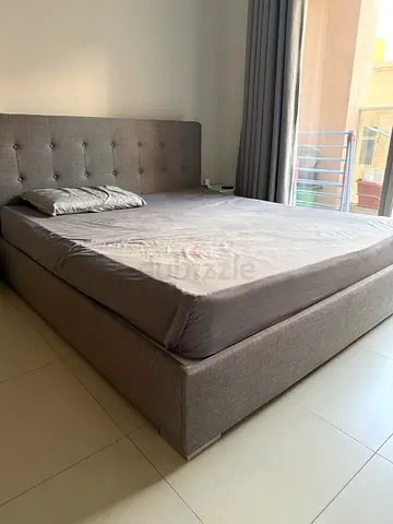 Grey king size upholstered bed with mattress and storage space below - available from 25th August
