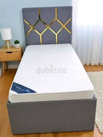 Single grey upholstered bed frame with mattress and gold-accent headboard