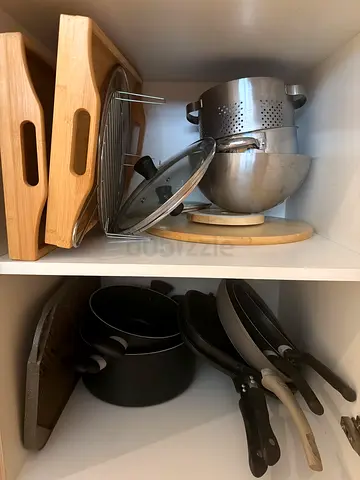 Mixed kitchen cookware appliances: non-stick pans, lids, colander and wooden trays