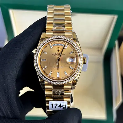 This is a Rolex Day-Date 40 in 18k yellow gold, featuring a diamond-set bezel and a champagne baguet