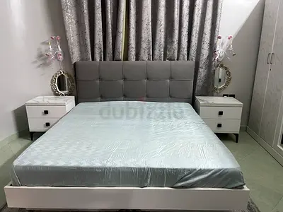 Modern white platform bed with grey upholstered headboard and 2 bedside tables and dresser