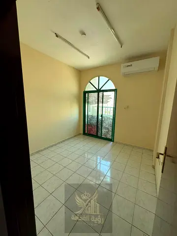 Two-bedroom apartment with living room for annual rent in Al Butina, Sharjah, featuring split AC and a balcony. Annual rent AED 25,000. Security depos