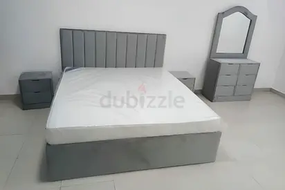 Grey upholstered bed frame with mattress, matching nightstands and dresser with mirror