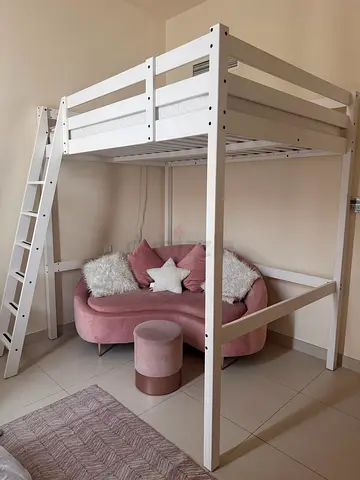 Girl bedroom furniture: white wooden loft bunk bed. Soft pink sofa, matching pouf and rug.