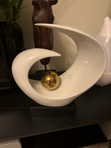 Modern white ceramic swirl sculpture with gold orb on black base