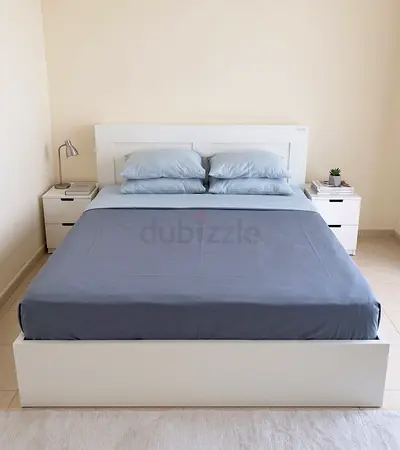White double bed frame with headboard and mattress and side cabinets