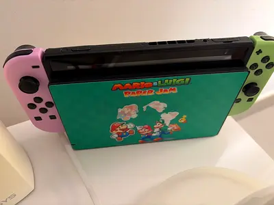Nintendo Switch console with Joy‑Cons (pink & green) and Mario & Luigi game case