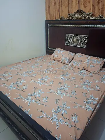 King size ornate wooden bed with mattress and floral bedsheet