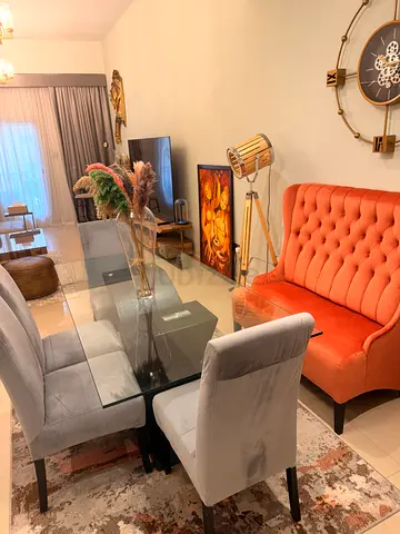 Glass Top Dining Table with 4 Grey Upholstered Chairs and 1 large orange lounge chair.