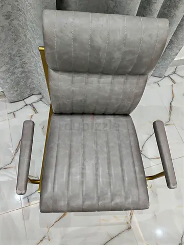 Grey upholstered swivel office chair with gold frame and armrests