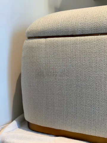 Beige upholstered storage ottoman with gold base