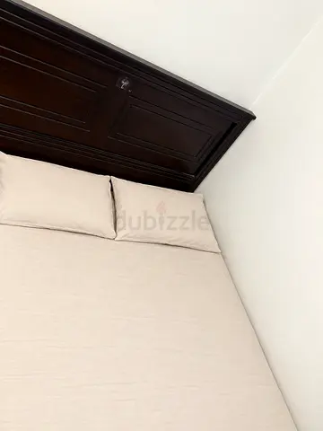Solid wood queen bed frame with beige mattress and linens