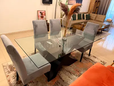 Glass Top Dining Table with 4 Grey Upholstered Chairs and 1 large orange lounge chair.