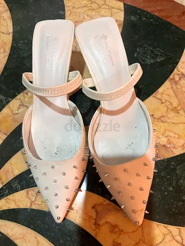 White high-heeled shoes with spikes, showing signs of heavy wear.