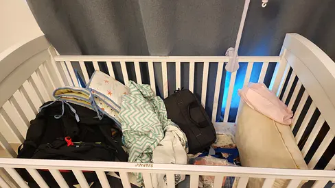 Unused white baby crib with mattress and bedding.