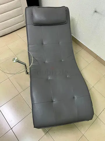 A modern grey faux leather chaise longue featuring an attached round glass side table and metal legs