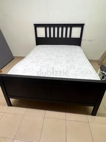 An IKEA "HEMNES" wooden bed frame in a black-brown finish, featuring a slatted headboard and a match