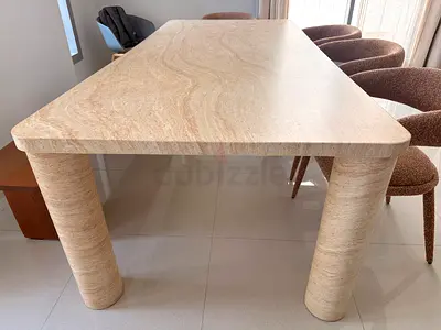 8 seats natural beige travertine dinning table, has rounded rectangular top with cylindrical legs.