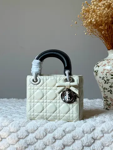Small white quilted leather handbag with black top handle and silver charm