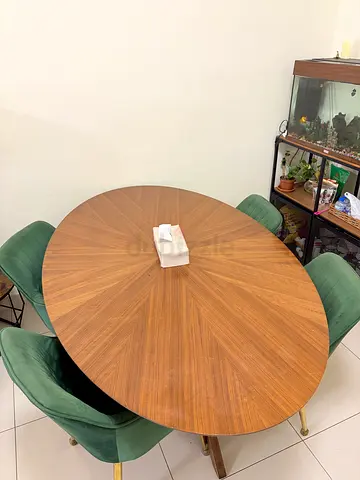 Round wooden dining table with 5 green velvet chairs.