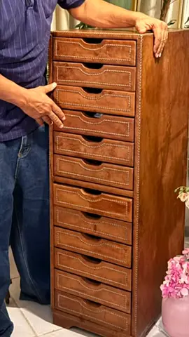 A tall wooden cabinet with leather detailing and 12 drawers—an elegant decorative piece.