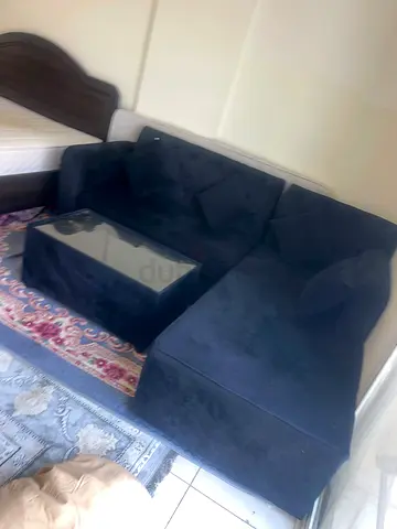 Dark blue L-shaped sofa with glass-top coffee table - good condition