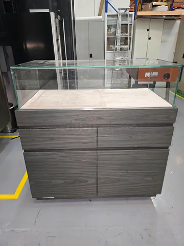 gray wooden display cabinet with a clear glass top, two small drawers, and a double-door