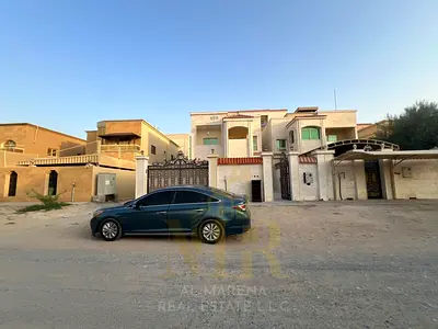 For Rent in Al Muwaihat 2, Ajman – Located next to the mosque, facing both a street and a side lane. Features two floors plus a roof terrace, 5 master