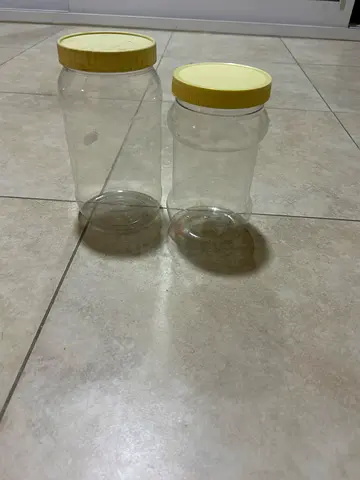 Two clear plastic storage jars with yellow screw lids