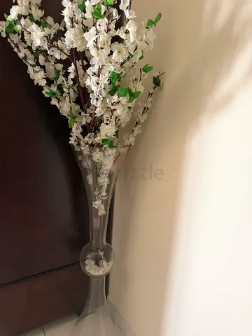 Tall clear glass floor vase with white artificial flowers