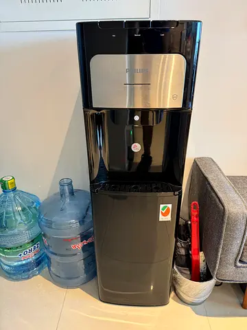 Black freestanding water dispenser with spare 19L bottles