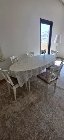 White wooden dining table with 6 chairs and oval tablecloth - good condition