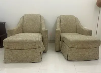 Pair of beige upholstered lounge chairs with ottoman-style seats