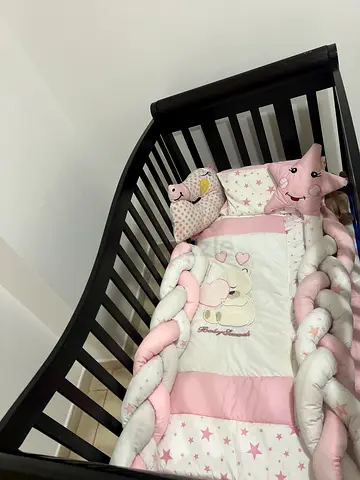 Dark wooden baby crib with pink bedding and braided bumper - good condition