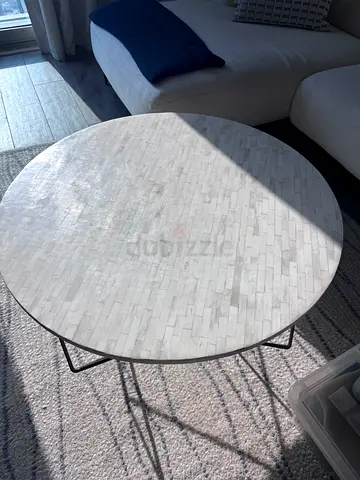Round marble-top coffee table with black metal legs and carpet