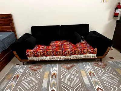 Black three-seater sofa cum bed with wooden frame and cushions