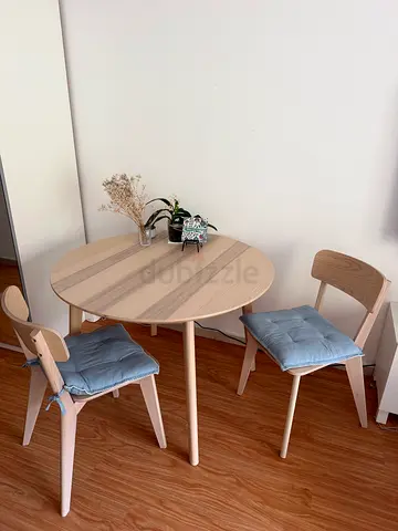 Ikea-style round dining table with 2 wooden chairs and cushions