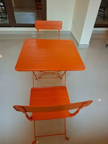 Orange metal outdoor bistro table with two matching folding chairs